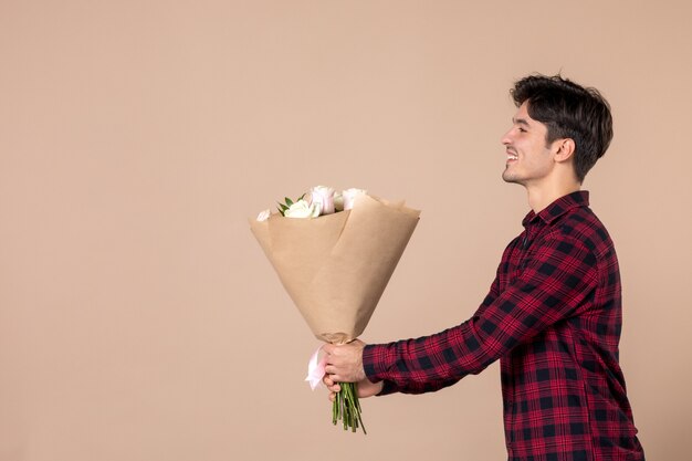 Front view young male giving beautiful flowers on brown wall