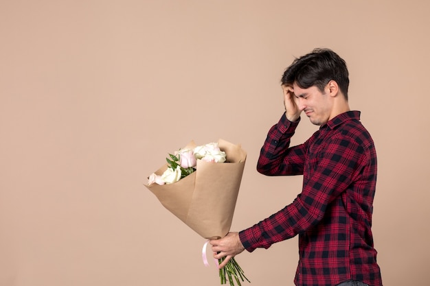茶色の壁に美しい花を与える正面図若い男性