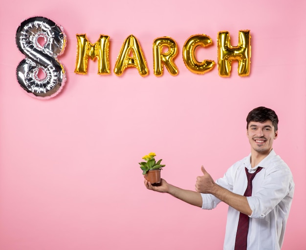 ピンクの背景パーティーフェミニンな平等女性の日男性の色の結婚の休日に3月のプレゼントとして誰かに小さな花を与える正面図若い男性