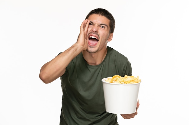 Front view young male in green t-shirt holding basket with potato cips and screaming on white wall lonely enjoyment film movie cinema