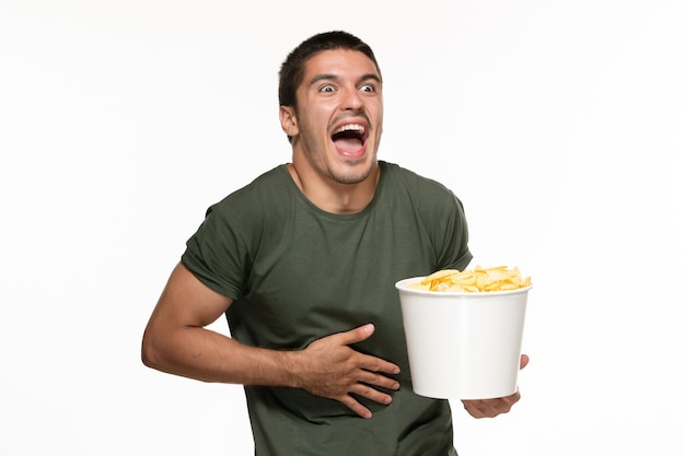 Front view young male in green t-shirt holding basket with potato cips watching movie on a white wall lonely film movie cinema