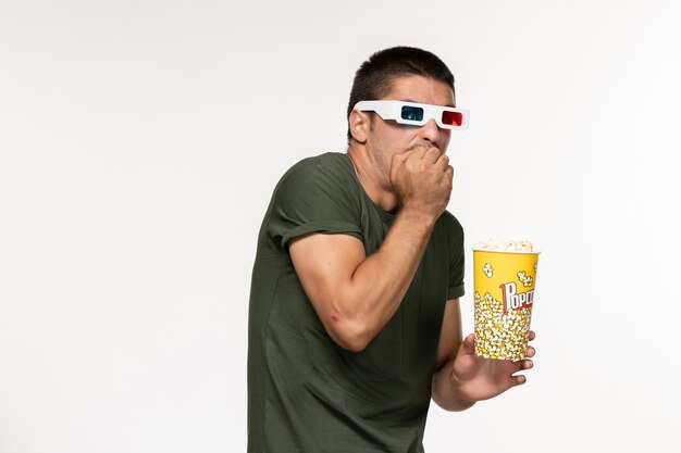 Front view young male in green t-shirt holding popcorn in d sunglasses watching movie on white wall film lonely cinema male movie