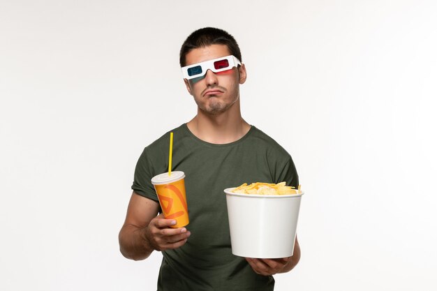 Вид спереди молодой мужчина в зеленой футболке, держащий картофельные чипсы и газировку в солнцезащитных очках на белом столе, фильм мужской одинокий фильм