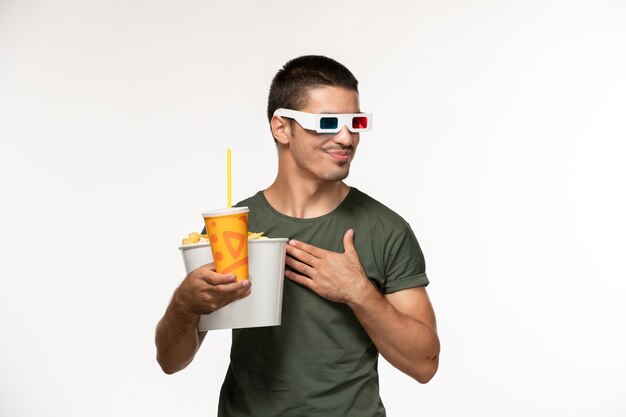 Вид спереди молодой мужчина в зеленой футболке, держащий картофельные чипсы с содовой в солнцезащитных очках -d на белом полу.