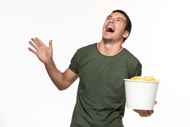 Вид спереди молодой мужчина в зеленой футболке, держащий картофельные чипсы и смотрящий фильм на белой стене одинокий кинотеатр