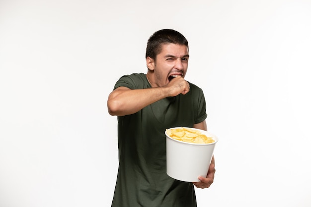 Вид спереди молодой мужчина в зеленой футболке, держащий картофельные чипсы, смотрит фильм на белой стене, человек одинокий фильм, кино