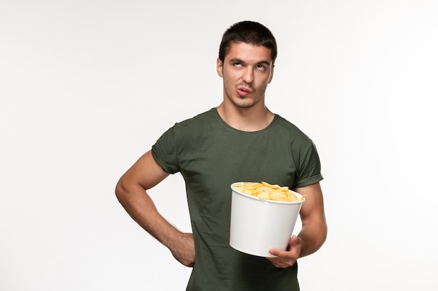 正面図緑のTシャツを着た若い男性、ライトホワイトの壁にジャガイモのcipsが付いていますフィルム人男性孤独な映画映画館