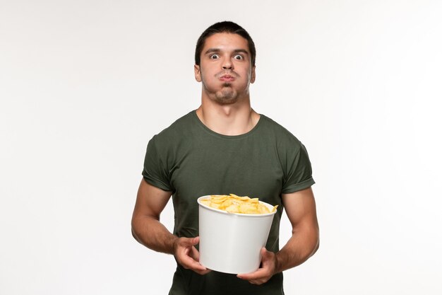 Вид спереди молодой мужчина в зеленой футболке с картофельными чипсами на белом столе кино человек мужчина одинокий кино