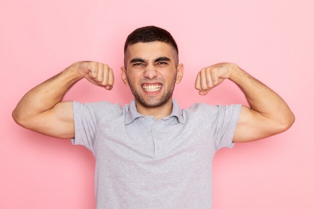 Front view young male in grey shirt flexing with both his hands on pink