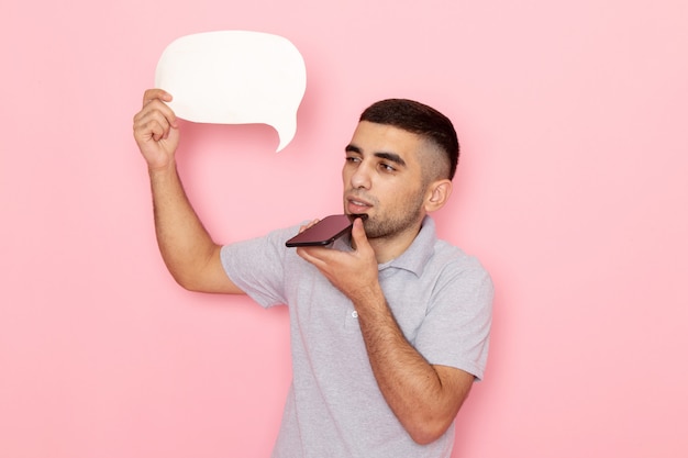 Front view young male in grey shirt holding white sign and talking on phone on pink