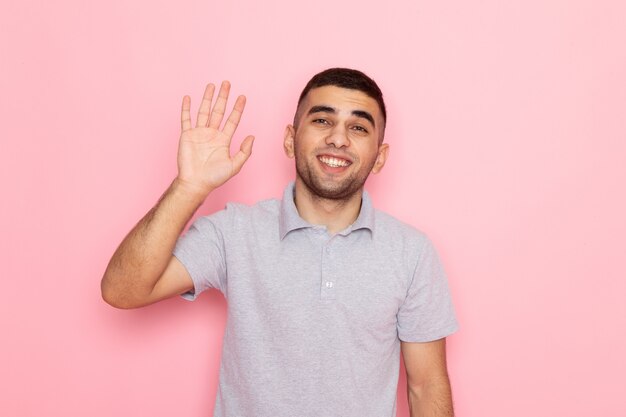 Front view young male in grey shirt posing and waving his hand on pink