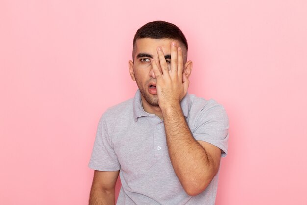 Front view young male in grey shirt posing with dissapointed expression on pink