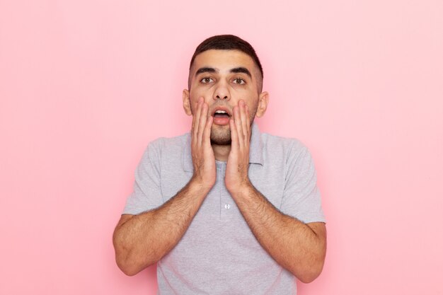 Front view young male in grey shirt posing with shocked expression on pink