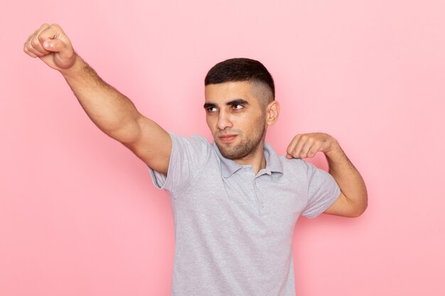 Front view young male in grey shirt posing with superhero sign on pink