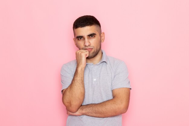 Front view young male in grey shirt posing with thinking stand on pink