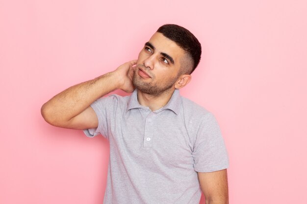 Front view young male in grey shirt posing with thinking stand on pink