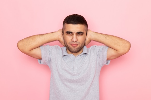 Front view young male in grey shirt shutting his ears on pink