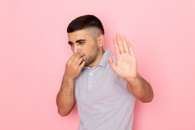 Front view young male in grey shirt shutting his nose on pink