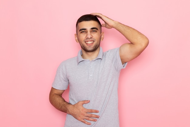 Front view young male in grey shirt smiling and holding his stomach on pink