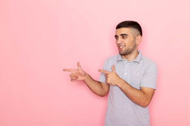 Front view young male in grey shirt smiling and pointing out with fingers on pink