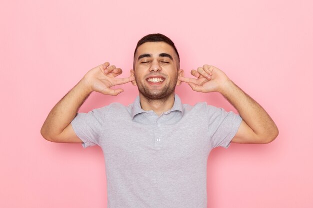 Front view young male in grey shirt smiling and shutting his ears on pink