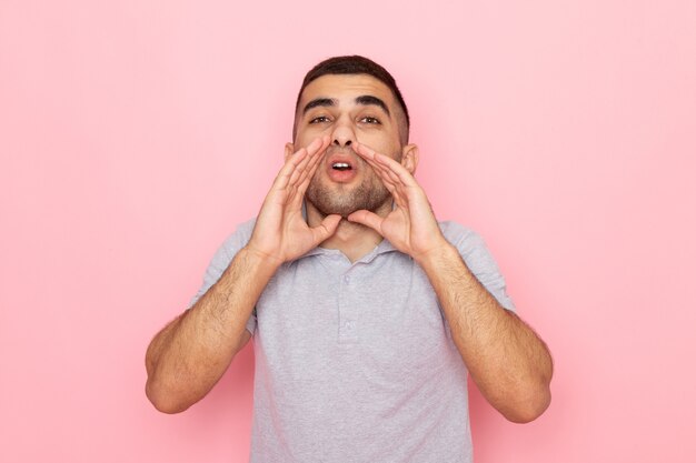 Front view young male in grey shirt whispering on pink