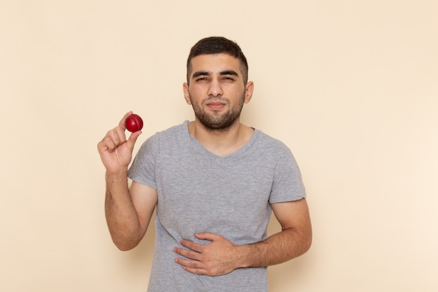 Front view young male in grey t-shirt and blue jeans holding sour plum on beige