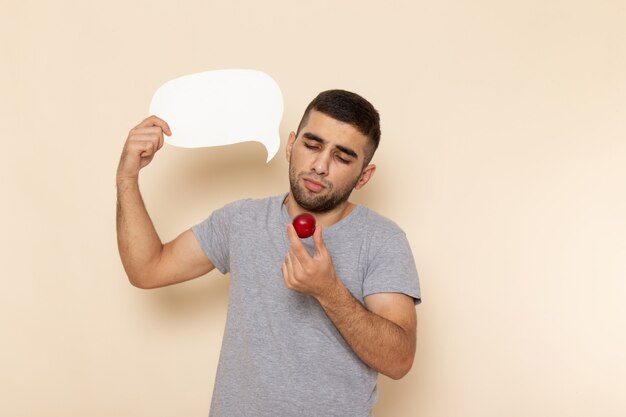 Front view young male in grey t-shirt and blue jeans holding white sign and plum on beige