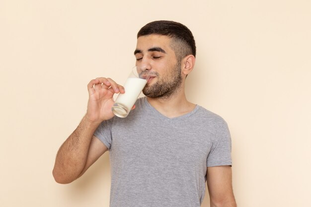 Front view young male in grey t-shirt drinking milk on beige