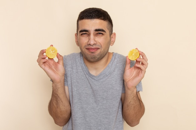 Front view young male in grey t-shirt eating sour lemon rings on beige