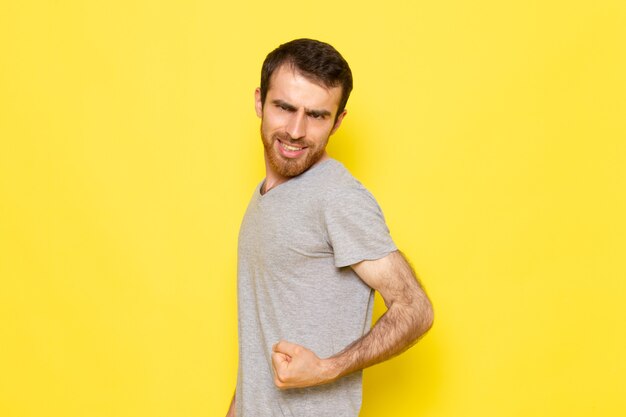 A front view young male in grey t-shirt flexing on the yellow wall man expression emotion color model