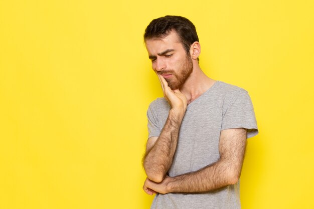 A front view young male in grey t-shirt having a toothache on the yellow wall man color model emotion clothes