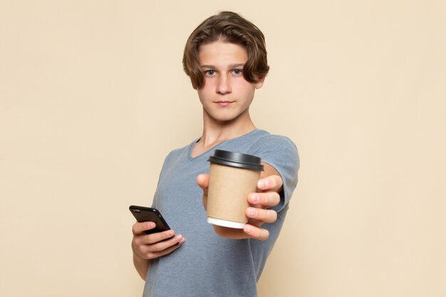 커피 컵과 전화를 들고 회색 티셔츠에 전면보기 젊은 남성