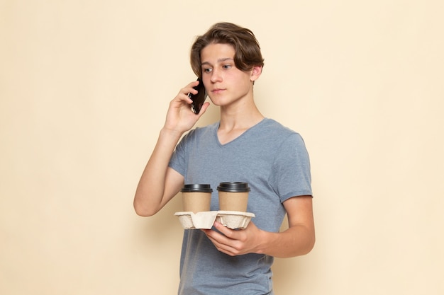 A front view young male in grey t-shirt holding coffee cups and talking on the phone