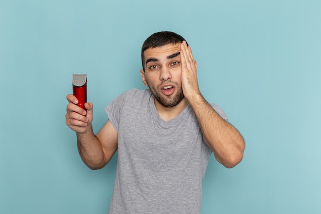 Free photo front view young male in grey t-shirt holding electric razor on the ice-blue beard foam razor shave