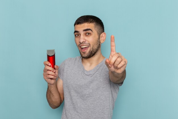 Front view young male in grey t-shirt holding electric razor on iced-blue beard foam hair razor shave