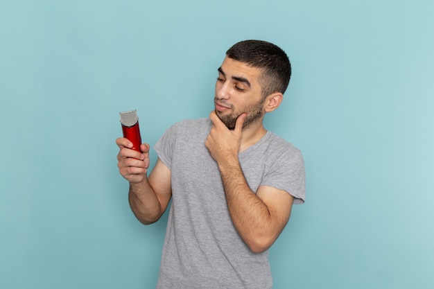 Front view young male in grey t-shirt holding electric razor thinking on the ice-blue beard foam hair razor shave