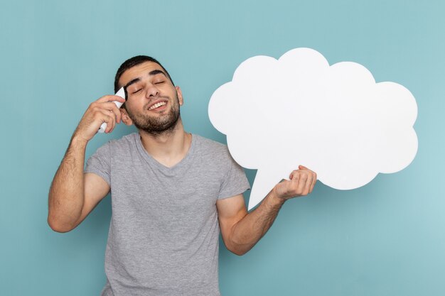 Front view young male in grey t-shirt holding electric razor with white sign on the ice-blue