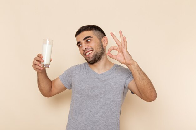 Front view young male in grey t-shirt holding glass of milk on beige