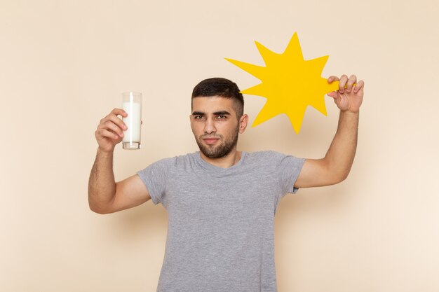 Вид спереди молодой мужчина в серой футболке держит стакан молочно-желтый знак на бежевом