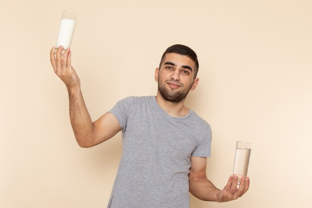 ベージュの水の牛乳のガラスを保持している灰色のtシャツの正面の若い男性