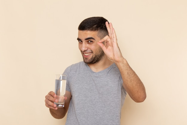 水のガラスを保持している灰色のtシャツの正面の若い男性