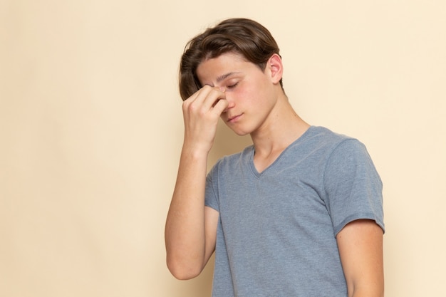 A front view young male in grey t-shirt holding his nose