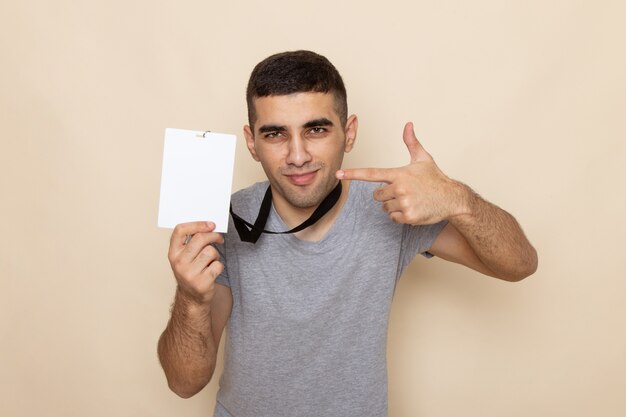 Front view young male in grey t-shirt holding identity card with light smile on beige