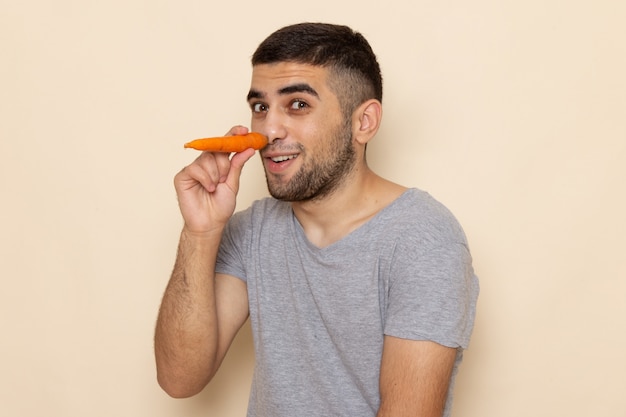 Front view young male in grey t-shirt holding orange carrot on beige