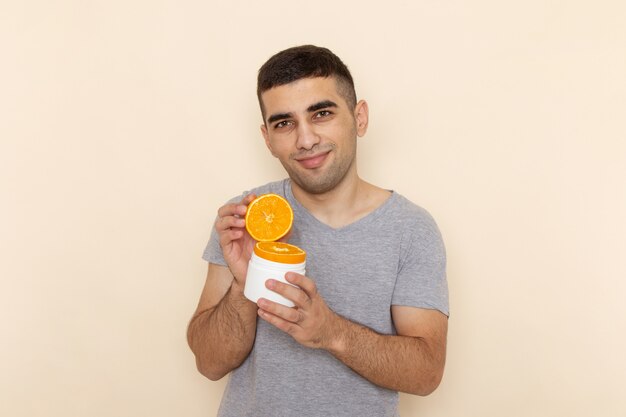 Front view young male in grey t-shirt holding orange slices with slight smile on beige