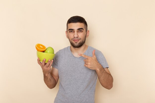 Front view young male in grey t-shirt holding plate with fruits on beige