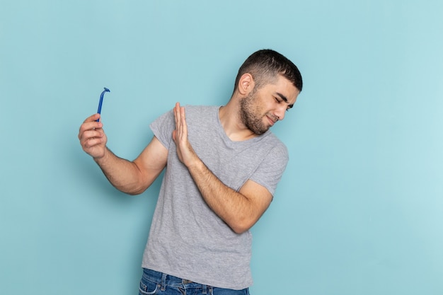 正面図灰色のTシャツを着た若い男性が青い机の上にかみそりを持ってひげを剃っている男性の髪の泡の色