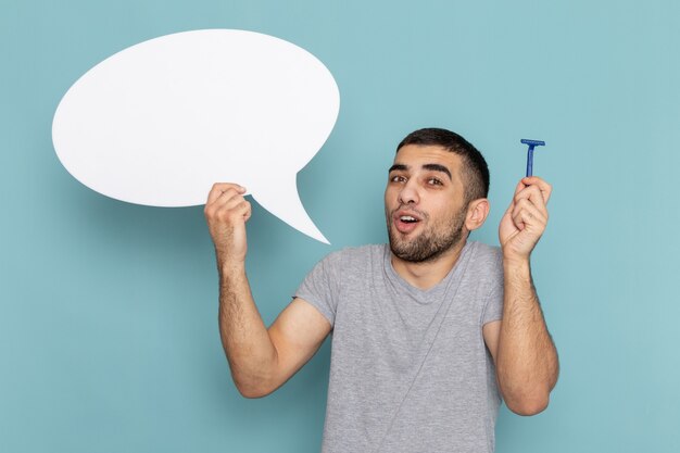 Front view young male in grey t-shirt holding razor and huge white sign on blue