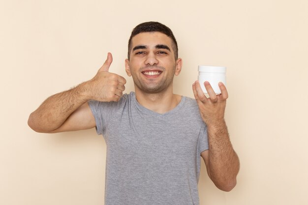 Front view young male in grey t-shirt holding white can with smile on beige